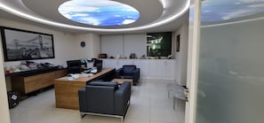 Un bureau moderne avec un bureau, des chaises, un canapé, une lucarne au plafond et un tableau encadré au mur.