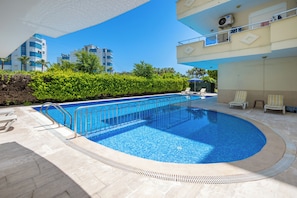 Une piscine dont le bord est revêtu de carrelage, entourée de chaises longues et d’une haie.