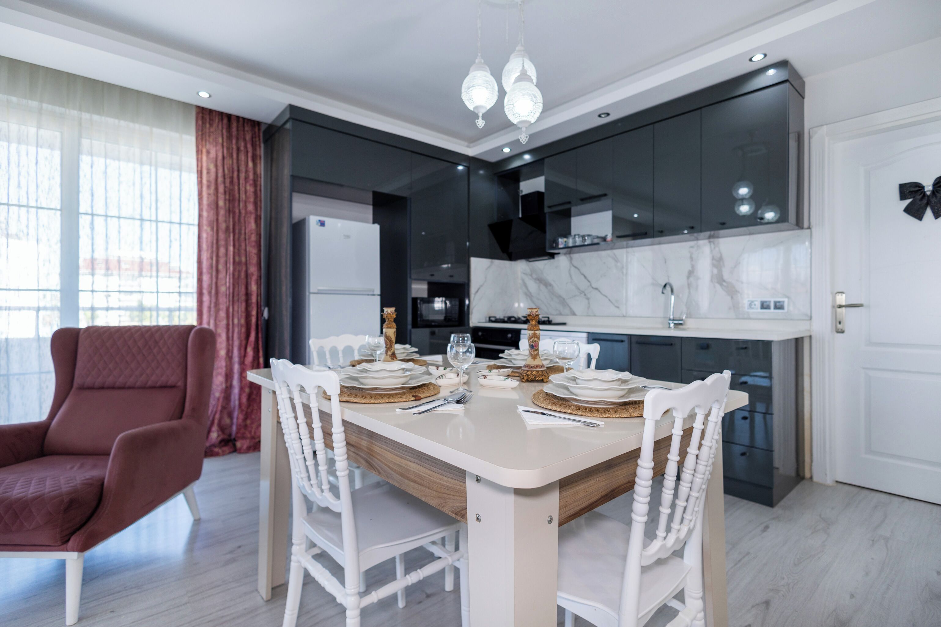 Una cocina moderna con armarios oscuros, encimera de mármol y comedor con una mesa blanca dispuesta para cuatro comensales.
