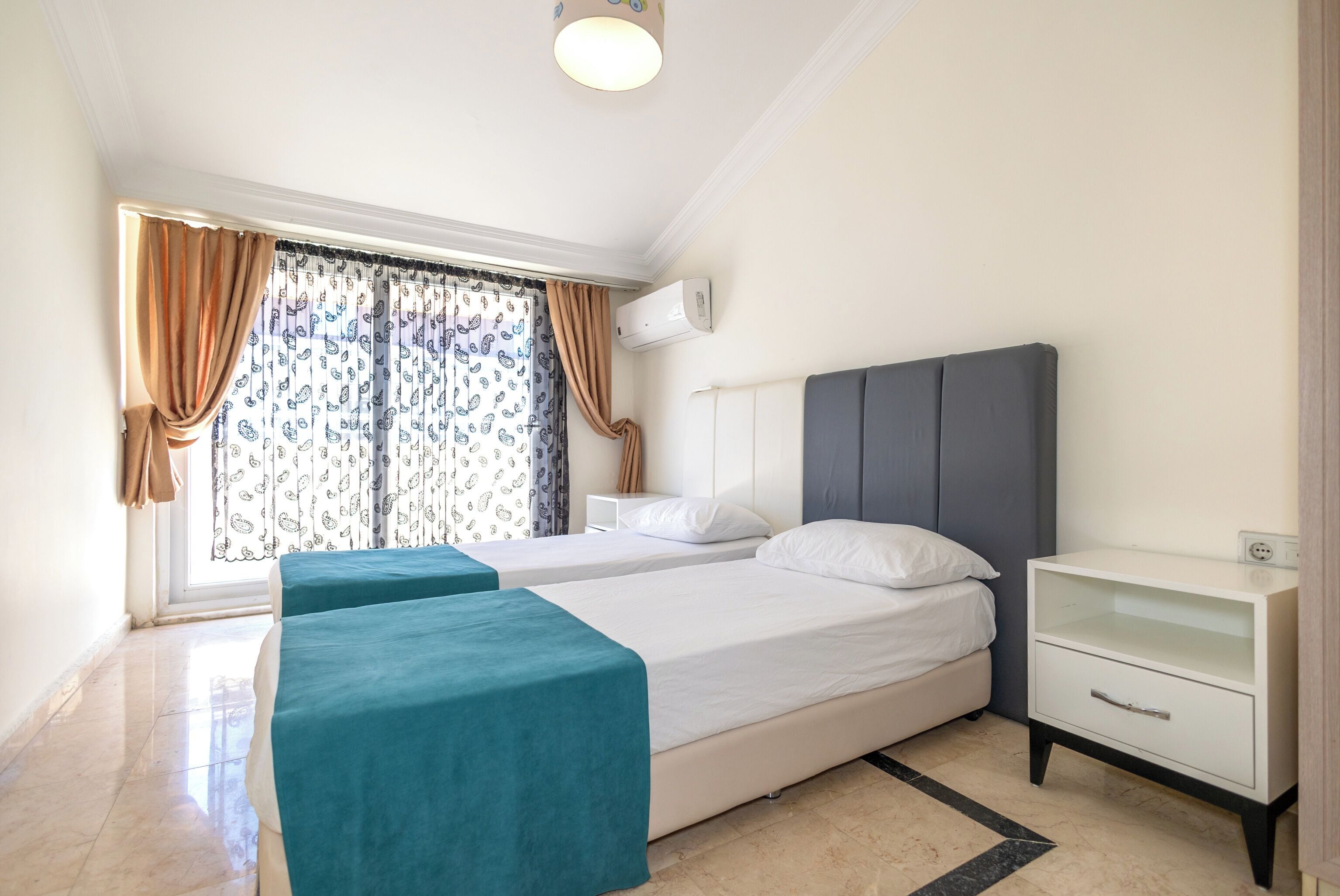 A bedroom with two beds, a nightstand, a window with curtains, and an air conditioning unit.