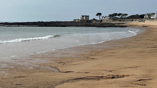 Une plage avec, en arrière-plan, une structure ressemblant à un château, un rivage sablonneux et des vagues calmes.