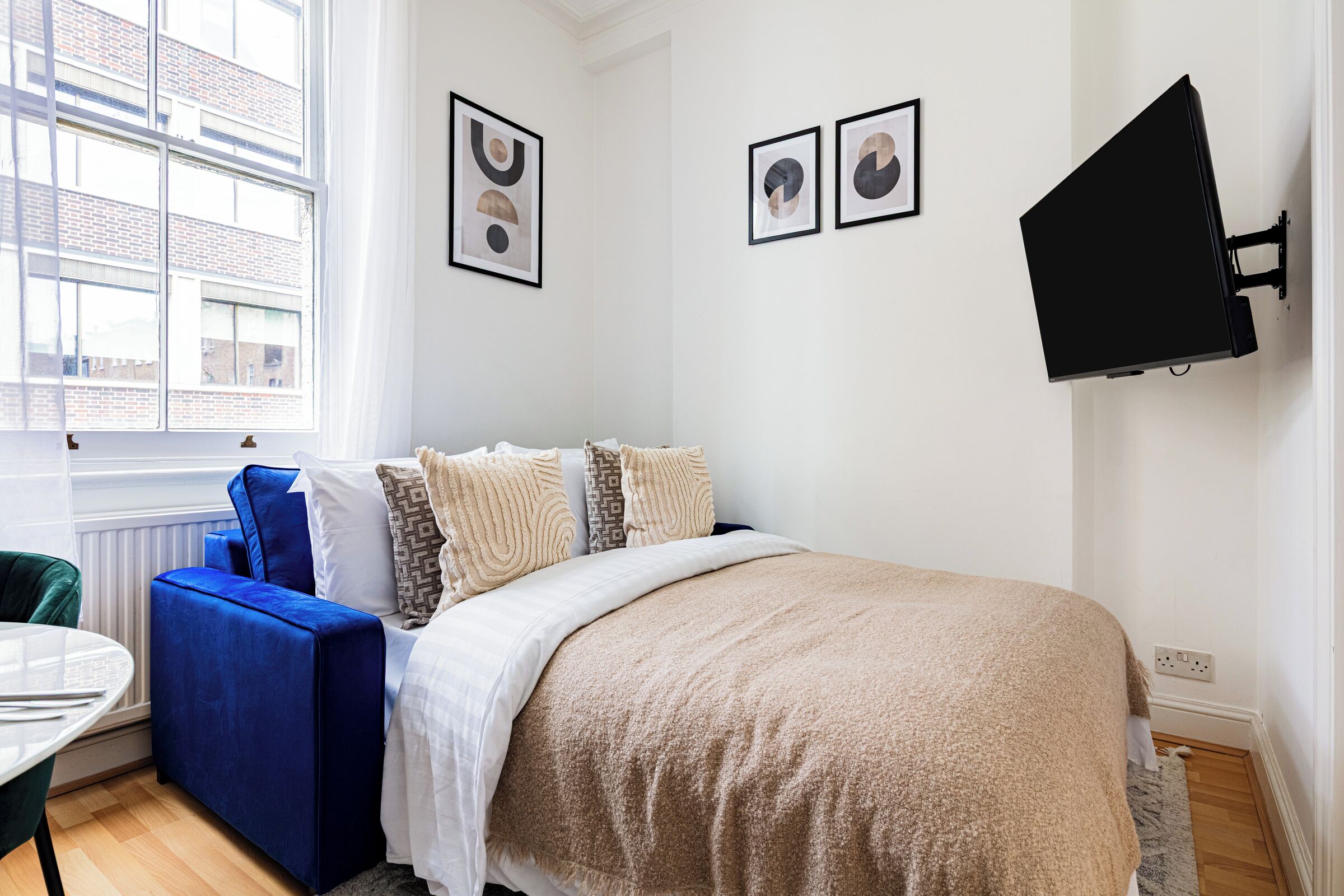 A bedroom with a bed, a blue chair, a desk, and a TV mounted on the wall.