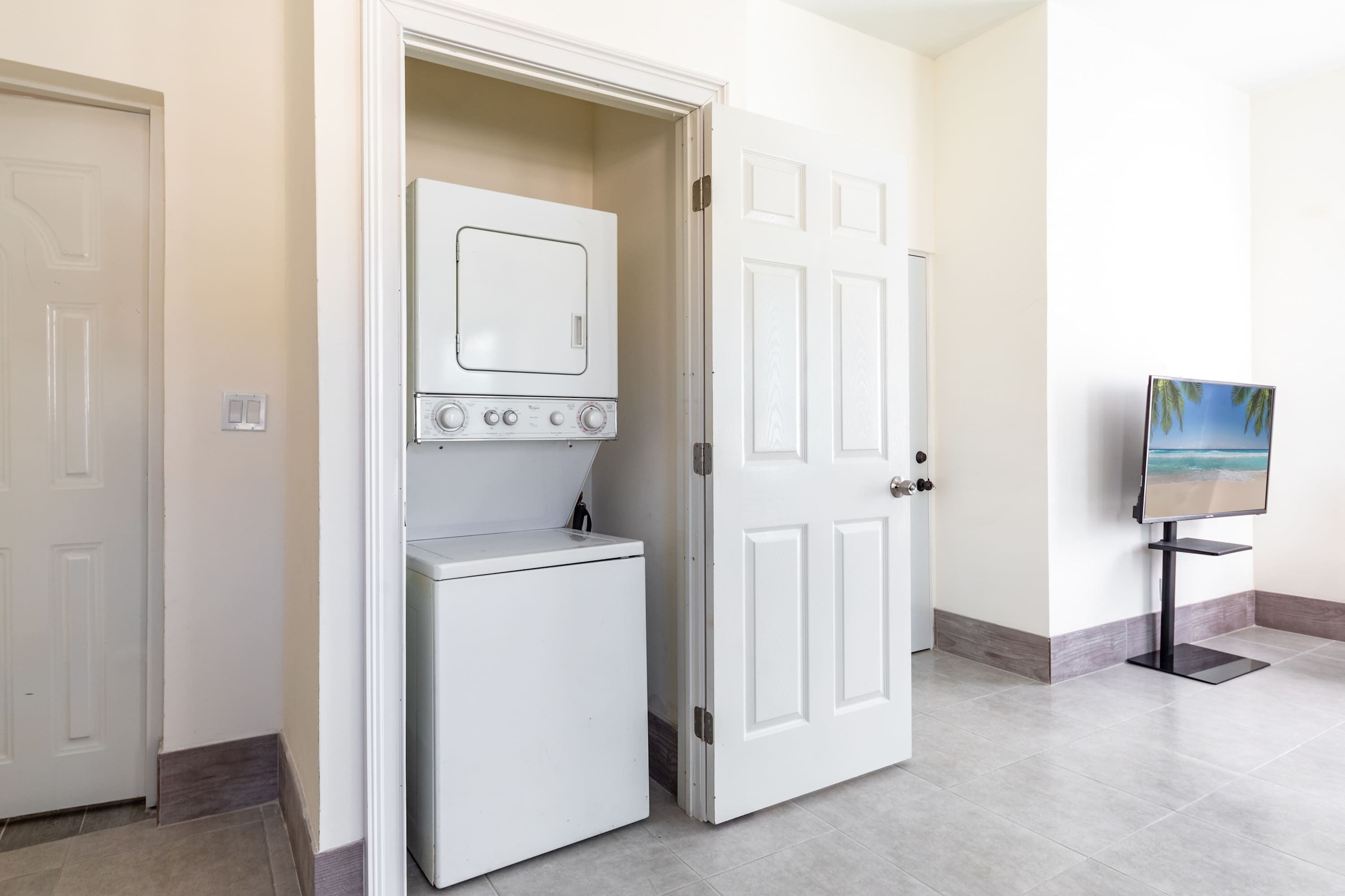 Une buanderie équipée d’un lave-linge et d’un sèche-linge, avec une porte et un téléviseur posé sur un meuble.