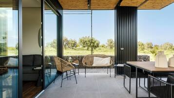 Un patio moderno al aire libre con paredes de vidrio, techo de madera y vistas a un paisaje cubierto de césped.