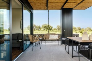 Un patio moderno al aire libre con paredes de vidrio, techo de madera y vistas a un paisaje cubierto de césped.