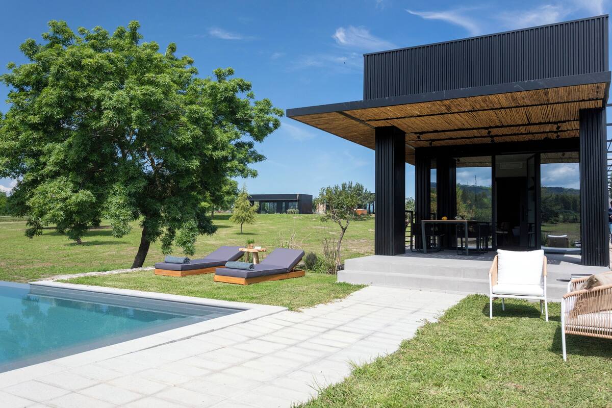Un área de piscina moderna al aire libre con sillones de descanso y una mesa de comedor.