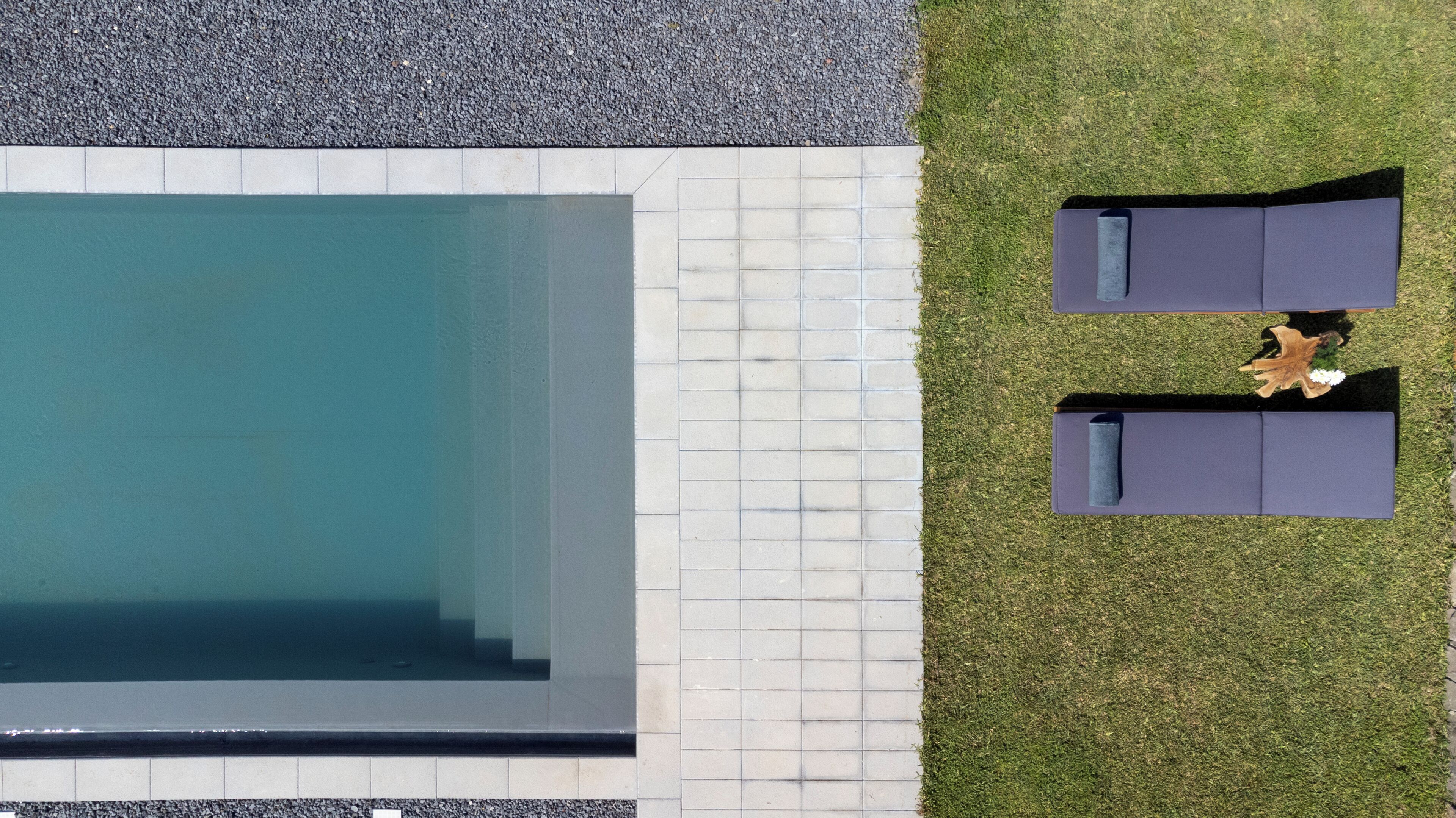 An aerial view of a swimming pool with a tiled deck, two lounge chairs, and a small garden area.
