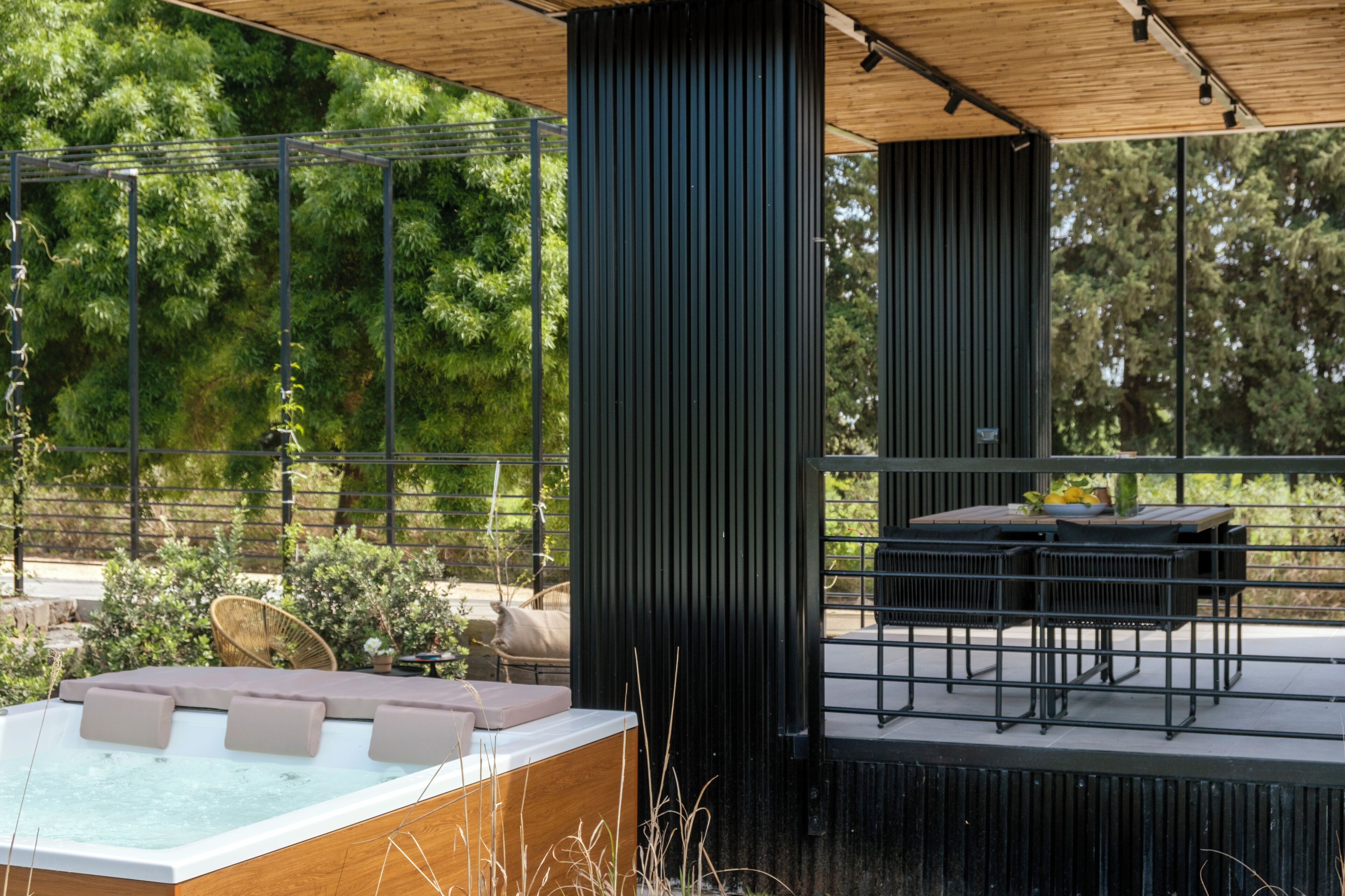 A modern outdoor patio with a hot tub, seating area, and a view of the surrounding greenery.