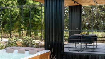 A modern outdoor patio with a hot tub, seating area, and a view of the surrounding greenery.