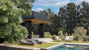 A modern outdoor pool area with a stone wall, lounge chairs, and a wooden deck. - Scorzamara Exclusive Country Lodges - Private Pool or Jacuzzi (Melilli)