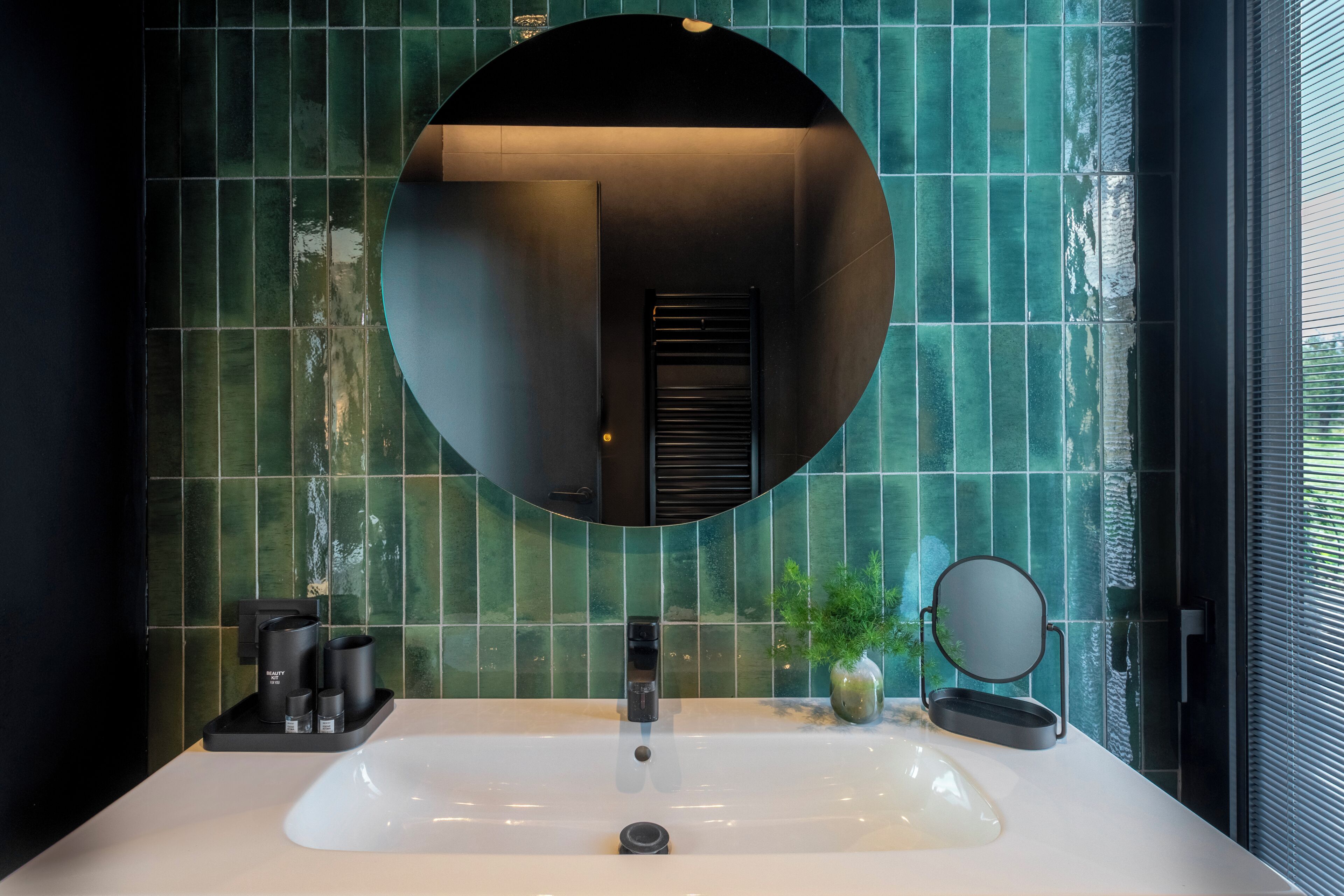 Un baño con un lavamanos grande, un espejo redondo y una planta en maceta.