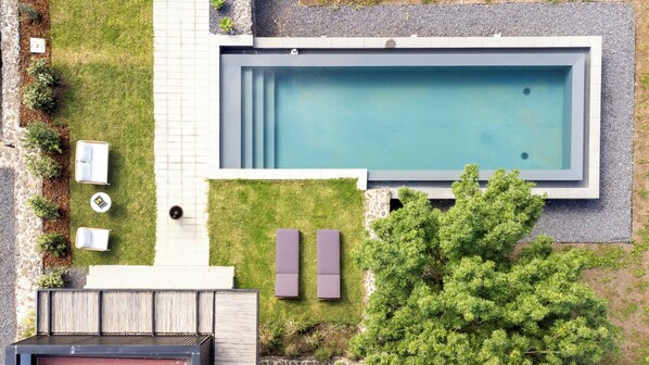 Une piscine extérieure moderne, agrémentée d’un chemin en pierre, de chaises longues et d’une petite terrasse.