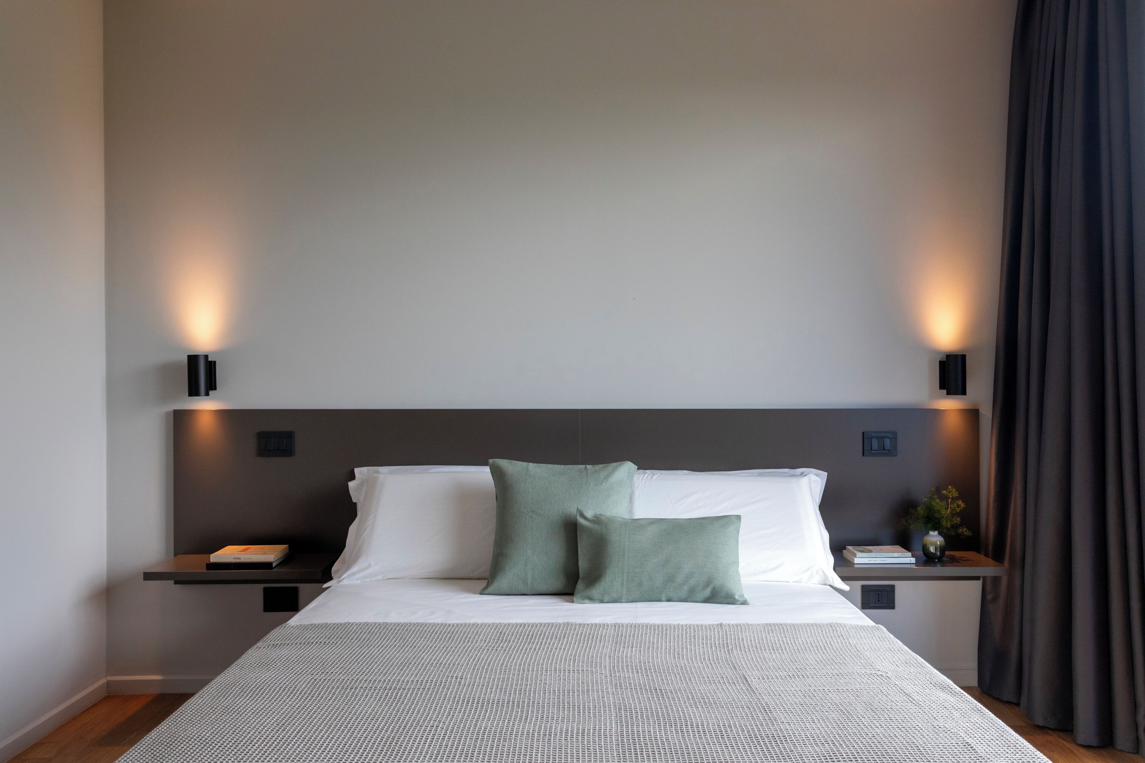A neatly arranged bedroom with a large bed, two bedside tables, and wall-mounted lighting.