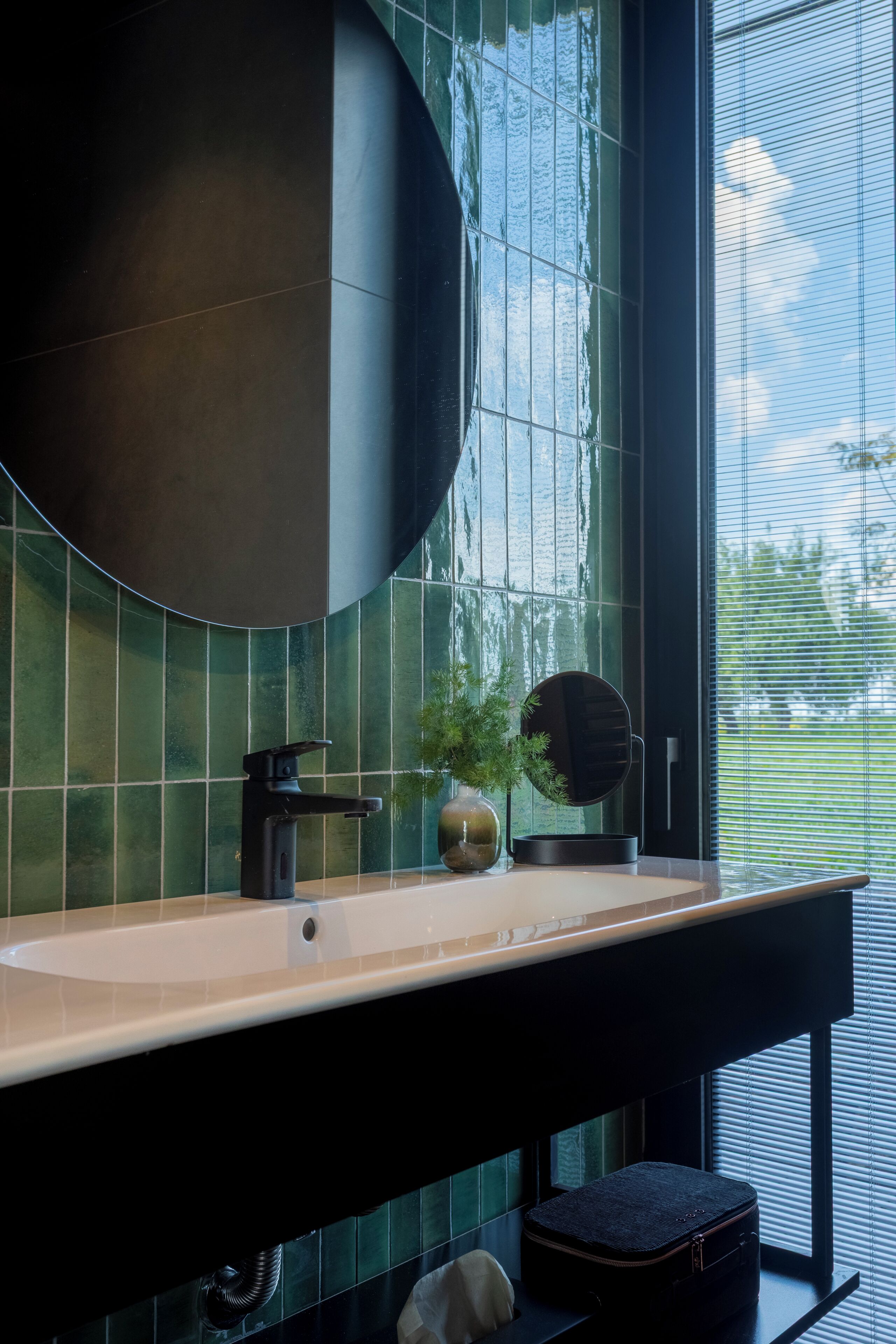 A bathroom with a large mirror, a sink, and a window with blinds.
