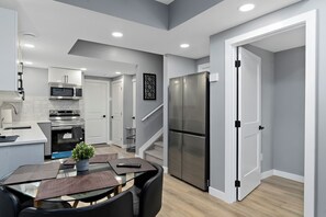 A modern kitchen with stainless steel appliances, a dining area with a glass table, and a staircase leading to another level.