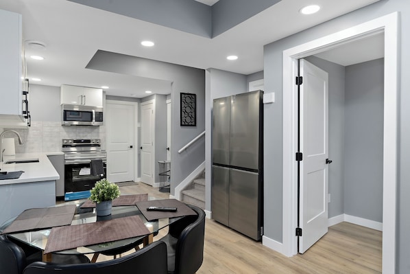 A modern kitchen with stainless steel appliances, a dining area with a glass table, and a staircase leading to another level.