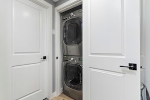 A laundry room with two stacked washers and dryers, white doors, and a small vent.