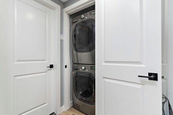 Une buanderie équipée de deux machines à laver et deux sèche-linge superposés, avec des portes blanches et une petite grille d’aération.