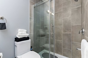 A bathroom with a glass-enclosed shower, a toilet, and a sink.