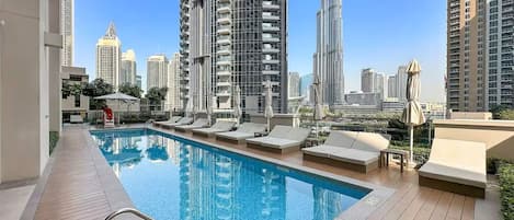 A rooftop pool with lounge chairs and umbrellas, surrounded by high-rise buildings.