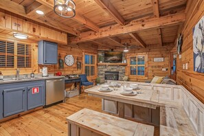L’intérieur d’une cabane comprenant une cuisine, un coin repas et une cheminée.