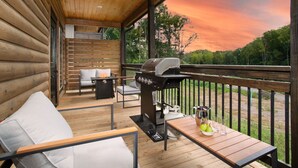 Eine überdachte Terrasse im Freien mit Grill, Sitzgelegenheit und Blick auf den Sonnenuntergang.