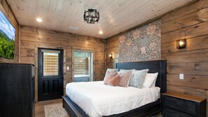Ein Schlafzimmer mit Holzbalkendecke, einem großen Bett mit vielen Kissen, einem Nachttisch und einer Wandleuchte.