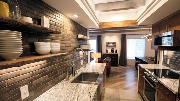 A modern kitchen with a marble countertop, dark brick backsplash, and stainless steel appliances.