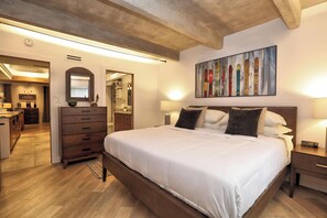 Ein Schlafzimmer mit einem großen Bett, einem Holz-Kopfteil, Nachttischen mit Lampen, einem Spiegel und einem Bild an der Wand.