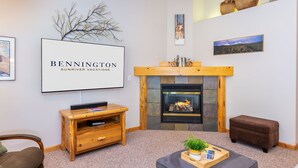 Un salon chaleureux avec une cheminée, un téléviseur fixé au mur et un panneau encadré sur lequel on peut lire : « BENNINGTON SUNRIVER VACATIONS ».