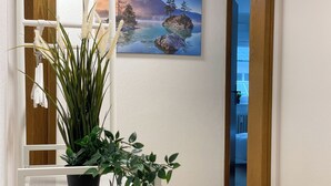 Una habitación con piso de madera, un banco blanco, una planta en maceta y un cuadro de un paisaje montañoso.