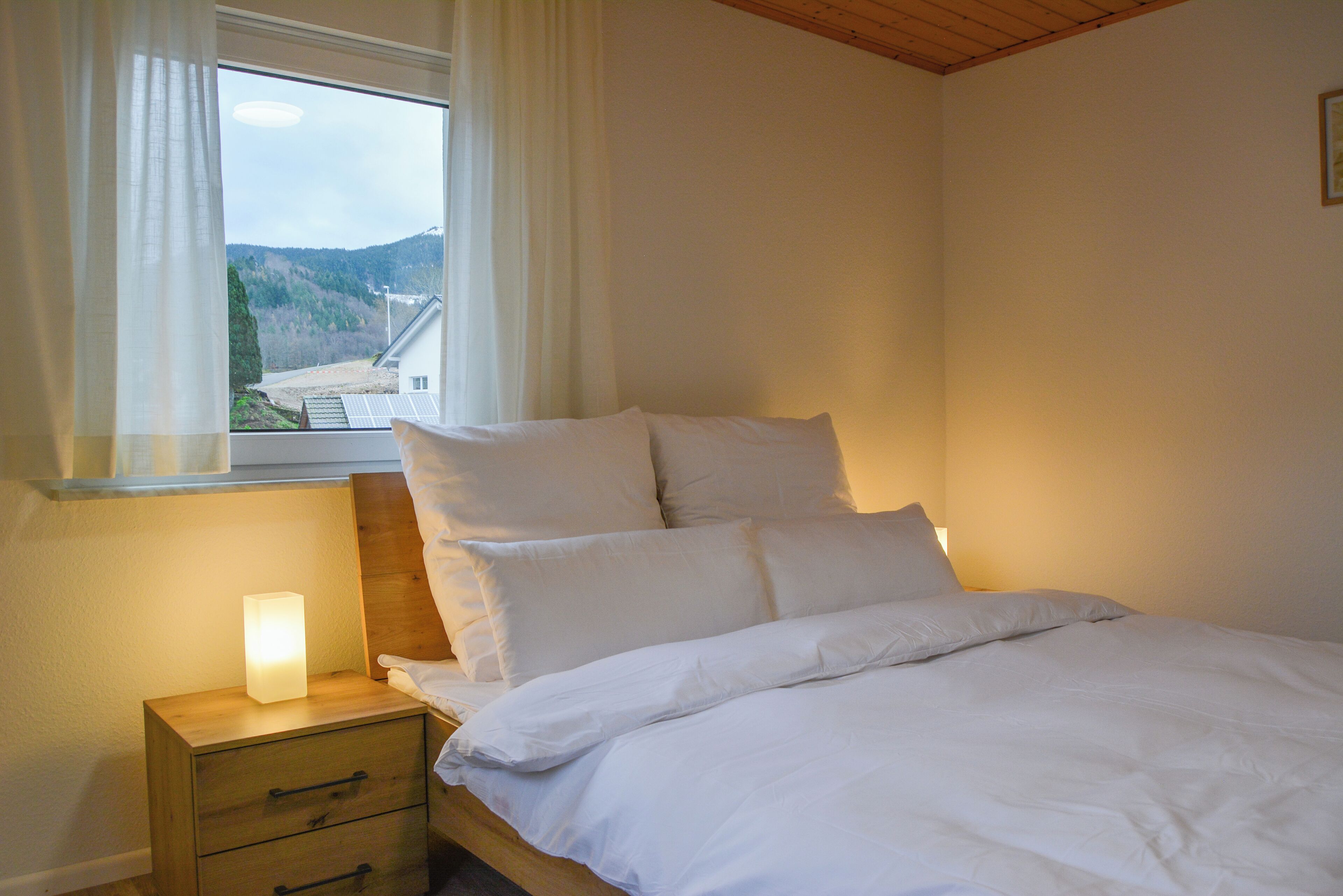 Ein Schlafzimmer mit einem Bett, einem Nachttisch, einer Nachttischlampe und einem Fenster mit Vorhängen.