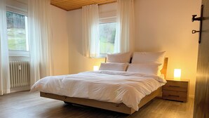 Una cama bien hecha con sábanas blancas, un cabecero de madera y una mesita de noche con una lámpara.