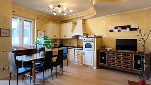 Een compacte keuken met witte kasten, een eettafel met stoelen, een televisie en een decoratieve plant.