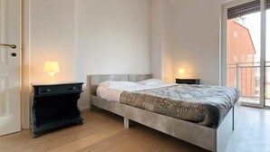 Een slaapkamer met een bed, twee nachtkastjes en een raam met uitzicht op een gebouw.