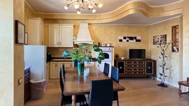 Een ruime keuken met een eethoek, houten kastjes, een grote tafel en een televisie.