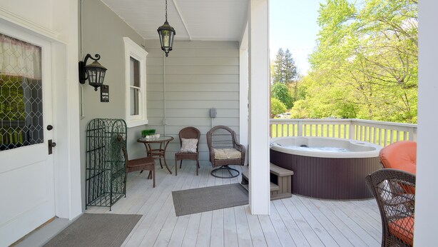 Une véranda abritée avec un jacuzzi, des fauteuils en osier et une lanterne suspendue.