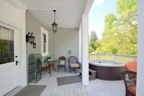 Eine überdachte Veranda mit Whirlpool, Korbstühlen und einer Hängelampe.
