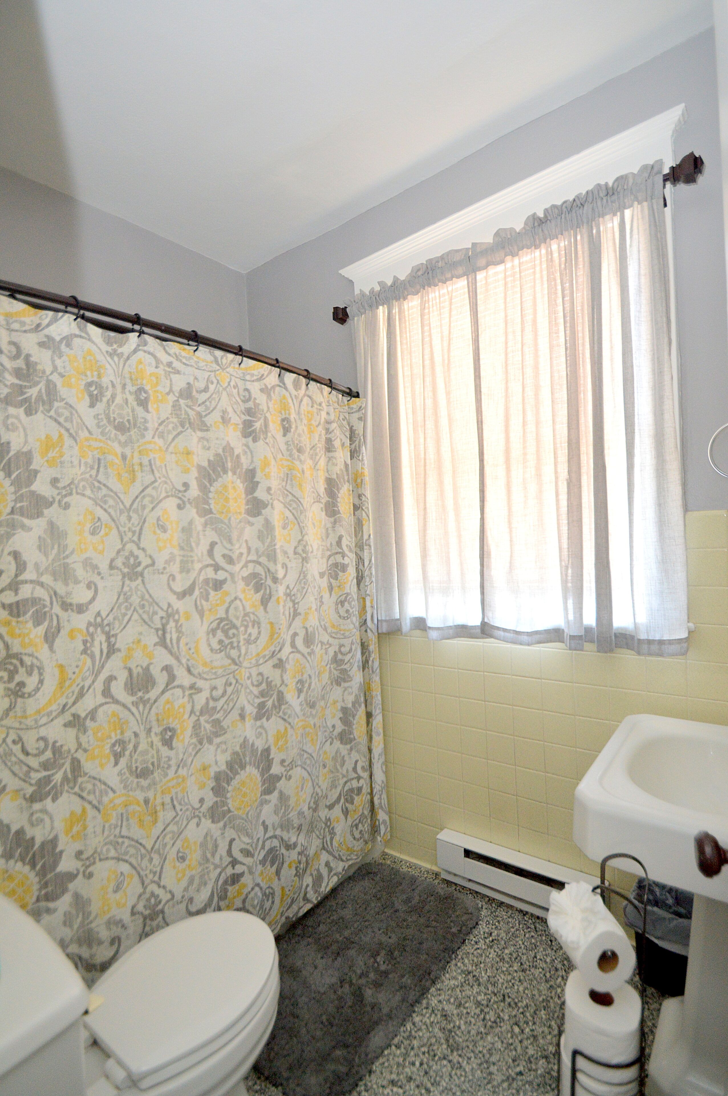 Ein Badezimmer mit Toilette, Duschvorhang und einem Fenster mit Vorhängen.