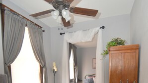 Une salle de bain avec une baignoire sur pieds, un ventilateur de plafond, une armoire en bois et une table de chevet agrémentée d’une plante.