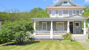 Une maison à deux étages avec un porche à l’avant, un drapeau et une boîte aux lettres.
