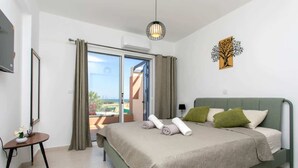A bedroom with a bed, a small table with a vase, a wall-mounted TV, and a view through a sliding door. - Harmony of Sea View & Nature,1BR (Polis Chrysochous)