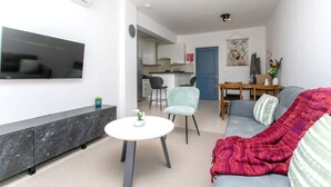 A modern living room with a flat-screen TV, a round coffee table, a grey sofa, and a dining area with a table and chairs. - Harmony of Sea View & Nature,1BR (Polis Chrysochous)