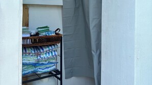 Un baño pequeño y cerrado con cortina de ducha, un estante con toallas dobladas y una cesta con artículos de aseo.