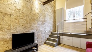 Un salon moderne avec un mur en pierre, un téléviseur à écran plat, un escalier et un fauteuil rouge.