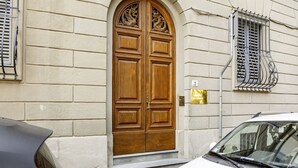 Une porte à deux battants en bois, surmontée d’une arche décorative, avec une grille métallique à la fenêtre et une petite plaque fixée au mur.