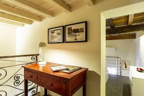 A wooden desk with a lamp and a magazine, a staircase with a metal railing, and two framed pictures on the wall.