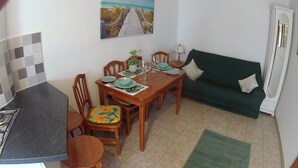A dining area with a wooden table set for four, a green sofa, and a kitchen area with a stove.