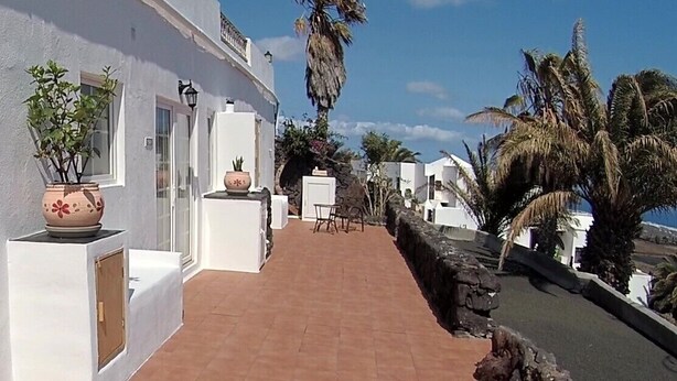 A white building with a tiled patio, outdoor furniture, and potted plants.