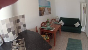 A compact kitchen with a dining area, a green sofa, and a painting of a beach on the wall.